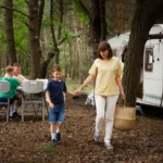 Une femme et deux enfants marchent dans les bois près d'un camping-car, entourés de verdure.