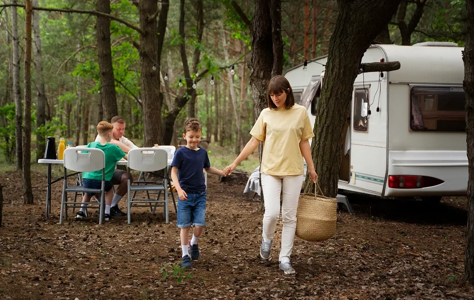 Une femme et deux enfants marchent dans les bois près d'un camping-car, entourés de verdure.