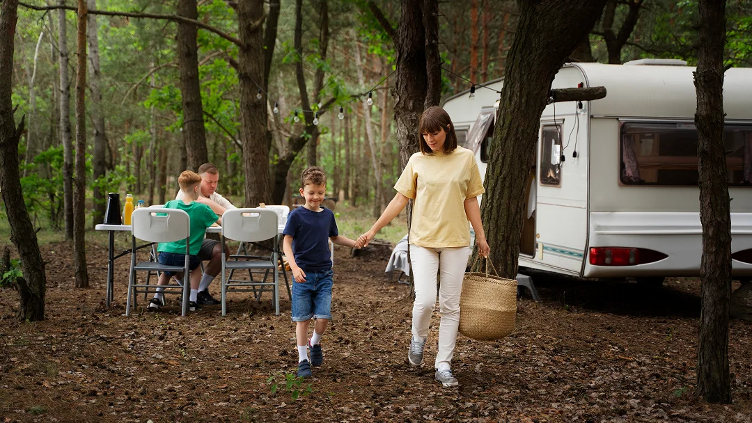 Une femme et deux enfants marchent dans les bois près d'un camping-car, entourés de verdure.