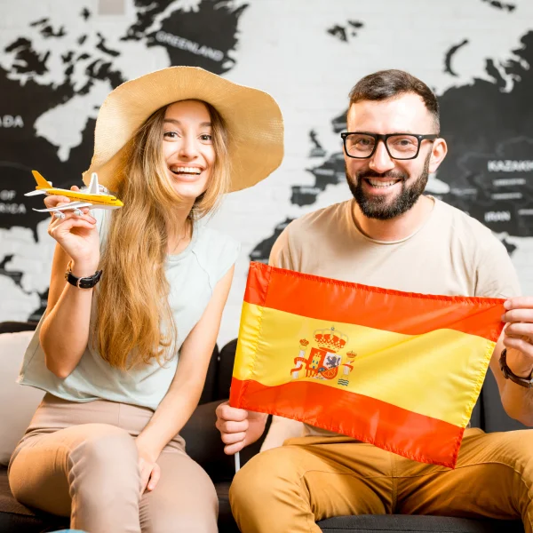 Un homme et une femme assis sur un canapé tenant un drapeau espagnol, illustrant un moment de convivialité en famille.